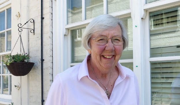 Photo of smiling Averil Mansfield with a hanging flower basket in background. 