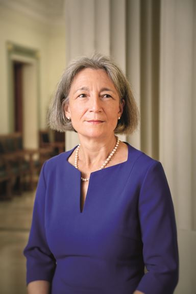 A photograph of Dame Clare Marx wearing a blue dress on the stairs in the old RCS England building. This serious of photos was used for her presidential portrait.